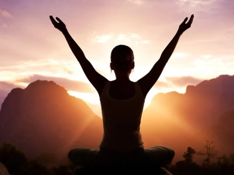 cr=t_0,w_100 A person sitting in the middle of a mountain with their arms raised.