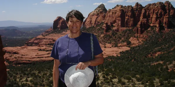 rs=w_600,h_300,cg_true A woman standing in front of some mountains holding onto a hat